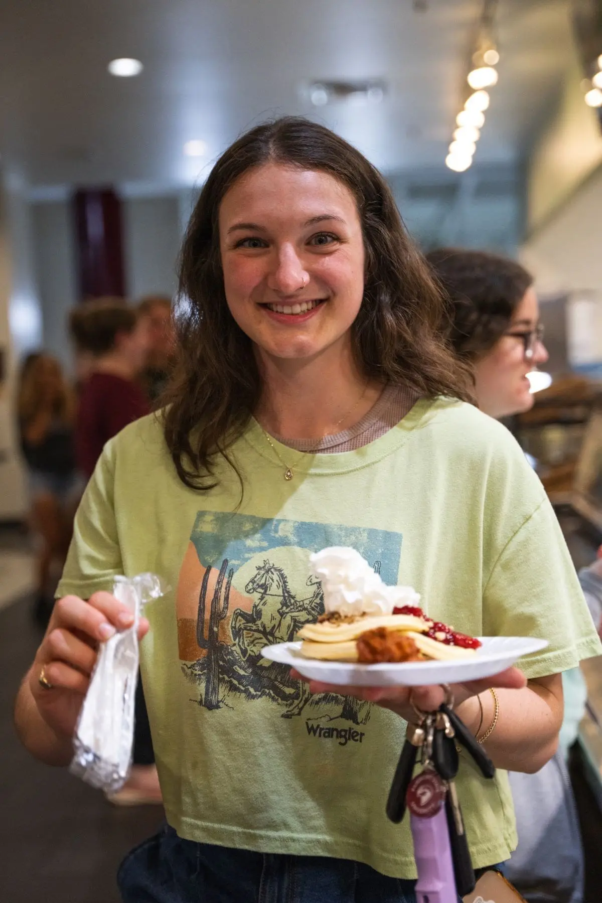 Student smiling while holding a plate for chicken and waffles standing in the middle of dining hall