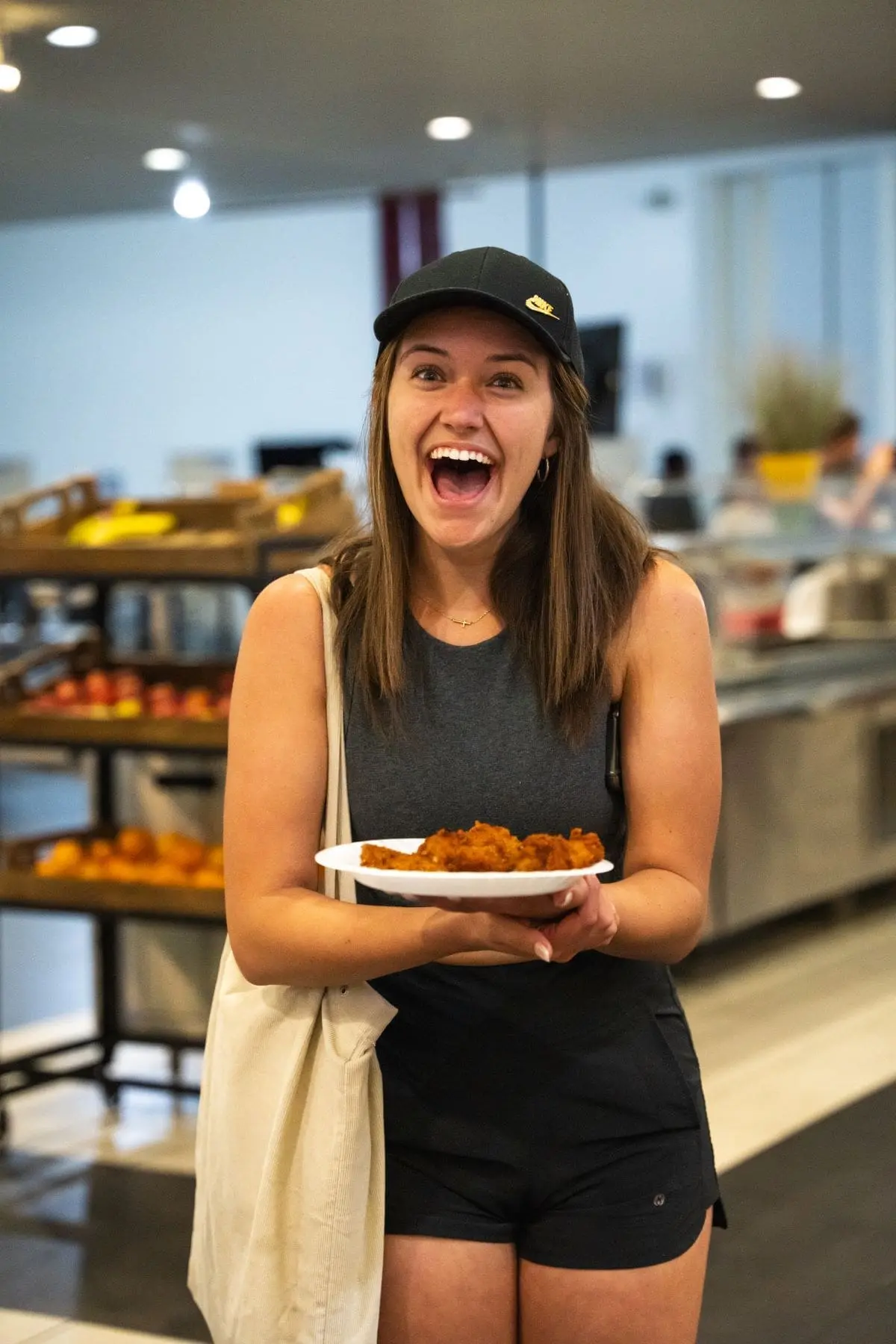 Student happily smiling while holding a plate for chicken tenders in cafeteria