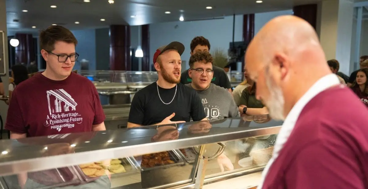 Students standing in line while employee works behind counter in cafeteria